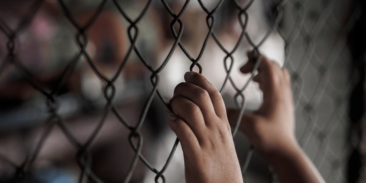 A child's hands grabbing a chain-linked fence, representing M&M International's Anti-Slavery & Human Trafficking Policy